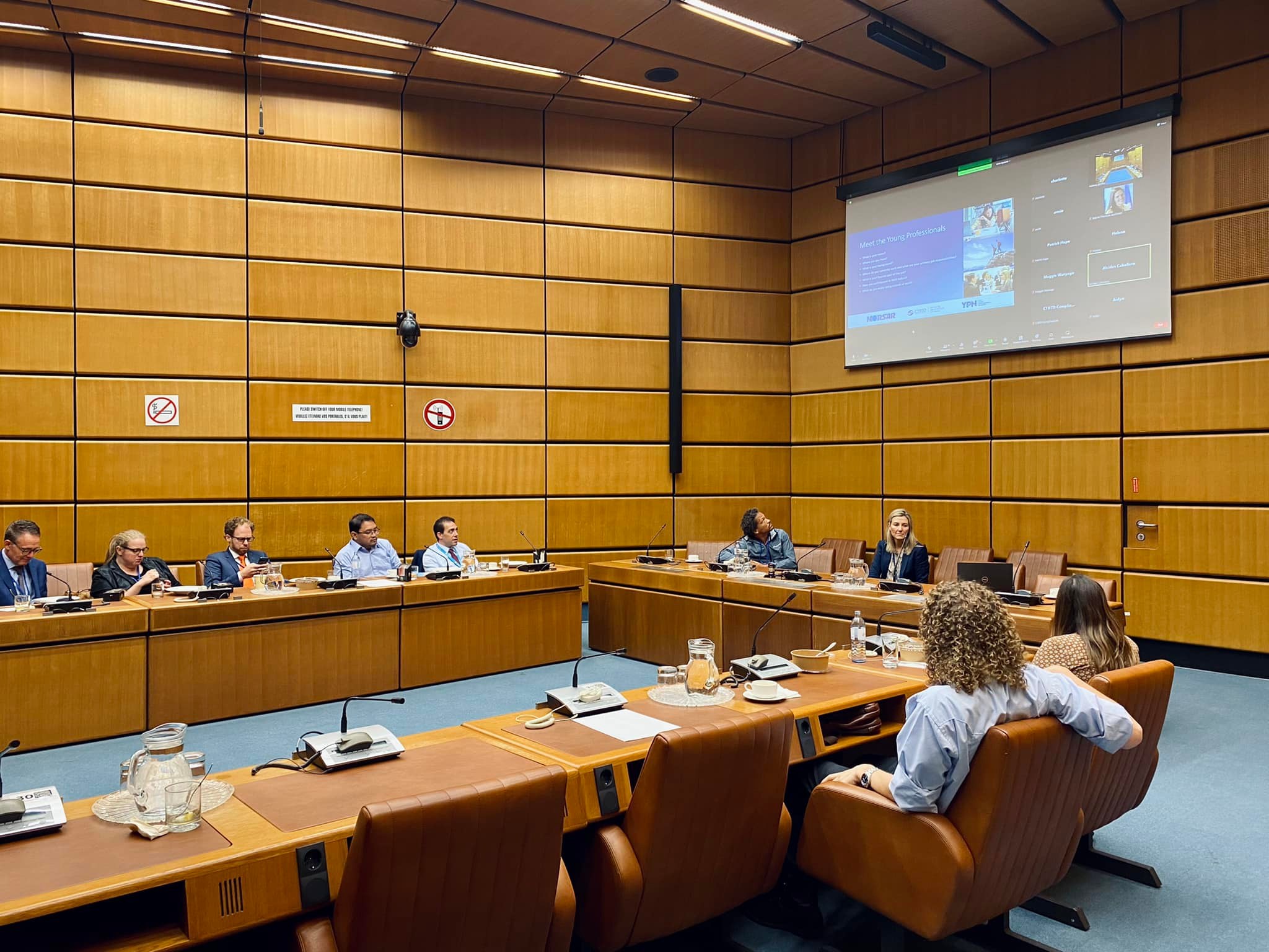 Network members in the conference room and on the screen. 